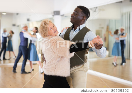 Elderly woman learning ballroom dancing in pair in dance studio Elderly woman learning ballroom dancing in pair in dance studio 86539302