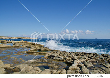 MARSAXLOKK, MALTA - 03 JAN, 2020: Traditional salt fields, Mediterranean Sea and small limestone hill in the background near Peter's pool MARSAXLOKK, MALTA - 03 JAN, 2020: Traditional salt fields, Mediterranean Sea and small limestone hill in the background near Peter's pool 86540269
