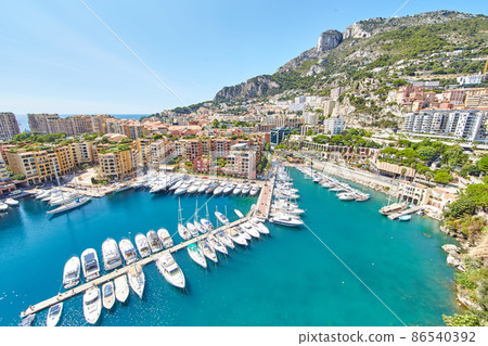 Panoramic image of Port Fontvieille - Monaco, top view from Monaco Ville, azur water, sun reflections on the water, harbour at sunny day, luxury apartments, a lot of yachts and boats, mountain 86540392