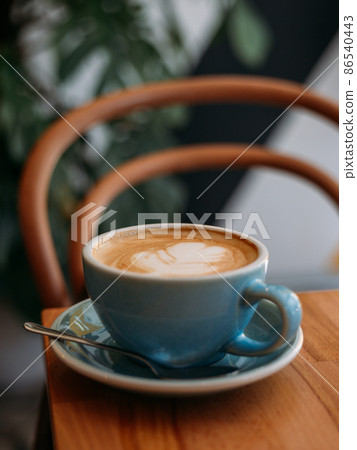 One Cup of cappuccino with latte art. Coffee in blue cup on wooden table in cafe. Concept of easy breakfast. One Cup of cappuccino with latte art. Coffee in blue cup on wooden table in cafe. Concept of easy breakfast. 86540443