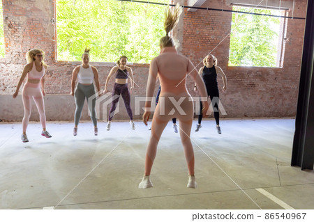 Young sporty women of different body types in sports clothing doing workout routine with a personal Young sporty women of different body types in sports clothing doing workout routine with a personal 86540967