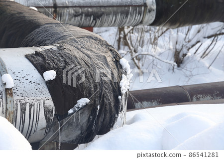 The main provides the city with hot water. Selective focus. The large pipes of the central heating system are covered with snow. Icicles on pipes. fuel crisis. Increasing the cost of heating. 86541281