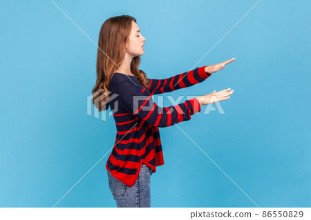 Side view portrait of blind woman in striped casual style sweater, walking alone with closed eyes in darkness, feeling disoriented confused, lost road. Indoor studio shot isolated on blue background. 86550829