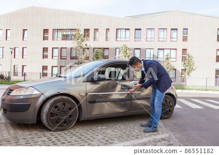 Profile of brunette man wearing jeans and jacket, car inspection for insurance claim the automobile, assesses the damage to the vehicle, examines carefully bent auto door. Outdoor shot. Profile of brunette man wearing jeans and jacket, car inspection for insurance claim the automobile, assesses the damage to the vehicle, examines carefully bent auto door. Outdoor shot. 86551182