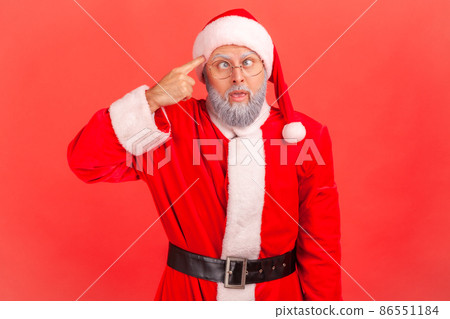 Elderly man with gray beard in santa claus costume crossed eyes, showing stupid gesture, looking at camera with condemnation and blaming for insane plan. Indoor studio shot isolated on red background. Elderly man with gray beard in santa claus costume crossed eyes, showing stupid gesture, looking at camera with condemnation and blaming for insane plan. Indoor studio shot isolated on red background. 86551184