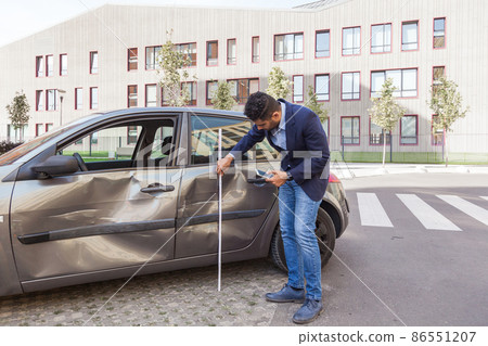 Insurance agent wearing jeans and jacket estimating car damage, assesses the damage to the automobile, dents and scratches at vehicle doors after wreck. Outdoor shot. 86551207