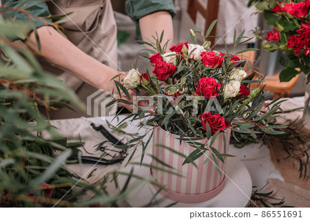 Florist make gift bouquets in hat boxes. Graceful female hands make a beautiful bouquet. Florist workplace. Small business concept. Front view. Flowers and accessories. Florist make gift bouquets in hat boxes. Graceful female hands make a beautiful bouquet. Florist workplace. Small business concept. Front view. Flowers and accessories. 86551691