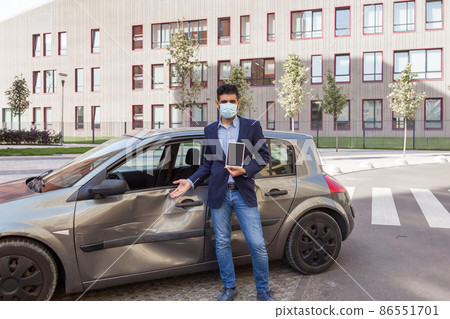 Young adult brunette insure agent wearing surgical medical mask, jacket and jeans, inspected dented car after road crash, showing dents and scratches on vehicle door. Outdoor shot. Young adult brunette insure agent wearing surgical medical mask, jacket and jeans, inspected dented car after road crash, showing dents and scratches on vehicle door. Outdoor shot. 86551701