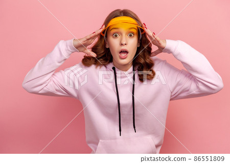 Portrait of surprised curly haired teenage girl in hoodie and yellow sun visor cap with big eyes and opened mouth looking at camera, shocking news. Indoor studio shot isolated on pink background 86551809