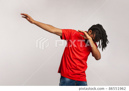 Portrait of young adult man with dreadlocks wearing red casual style T-shirt, standing in dab dance pose, internet meme, celebrating success. Indoor studio shot isolated on gray background. 86551962