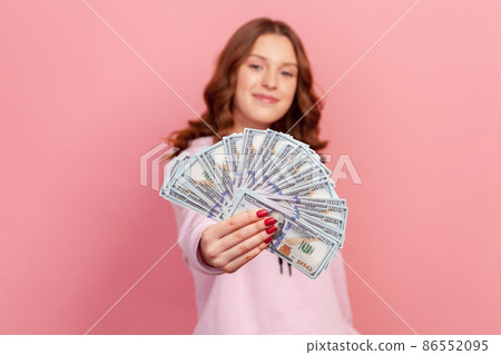 Portrait of satisfied curly haired young female lottery winner showing bunch of dollar banknotes at camera, profit and finance. Indoor studio shot isolated on pink background Portrait of satisfied curly haired young female lottery winner showing bunch of dollar banknotes at camera, profit and finance. Indoor studio shot isolated on pink background 86552095