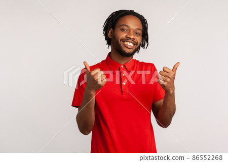 Attractive bearded man with dreadlocks wearing red casual style T-shirt, showing thumbs up, approval sign, satisfied with service, good feedback. Indoor studio shot isolated on gray background. 86552268