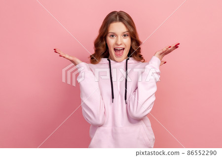 Portrait of extremely surprised teen girl in hoodie looking at camera with big eyes and open mouth, shocked with sudden victory. Indoor studio shot, isolated on pink background 86552290