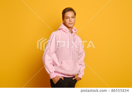 Stylish young man in pink sweatshot with hood posing over yellow studio background Stylish young man in pink sweatshot with hood posing over yellow studio background 86555834