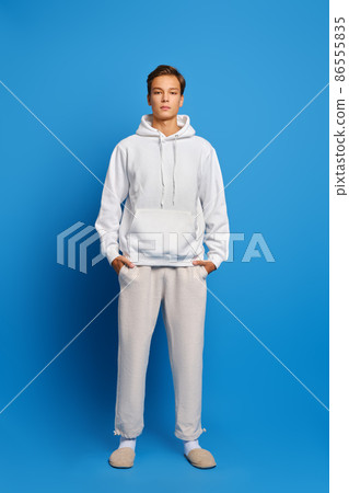 Attractive stylish man wearing white sweatshirt and sweatpants standing over blue studio background 86555835