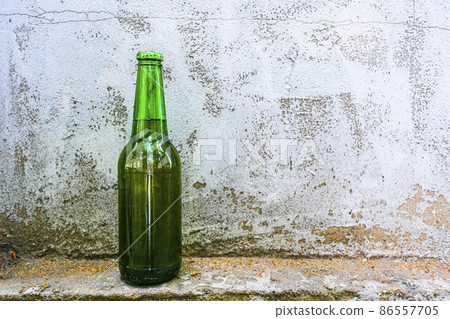 A bottle of beer stands against an old concrete wall A bottle of beer stands against an old concrete wall 86557705
