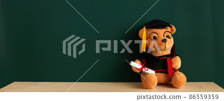Teddy bear with graduation hat and diploma in front of green chalkboard. Graduation concept Teddy bear with graduation hat and diploma in front of green chalkboard. Graduation concept 86559359