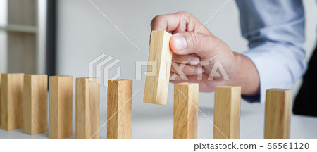 Risk and strategy in business, Close up of business woman hand gambling placing wooden block on a line of domino 86561120