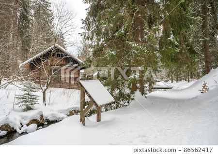 winter snowy forest in a mountain landscape with a stream and a cottage 86562417