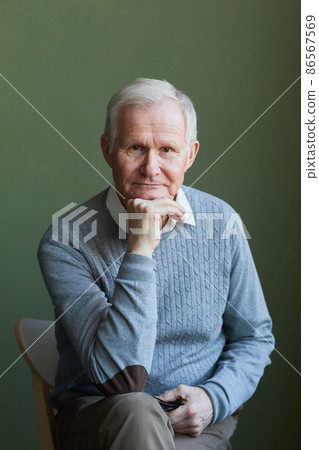 Serious elderly man in light blue pullover sitting on chair Serious elderly man in light blue pullover sitting on chair 86567569