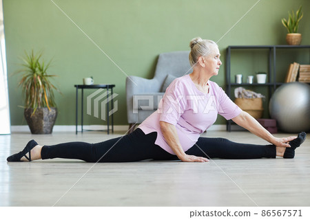 Side view of active senior female in sportswear sitting in twine on the floor Side view of active senior female in sportswear sitting in twine on the floor 86567571