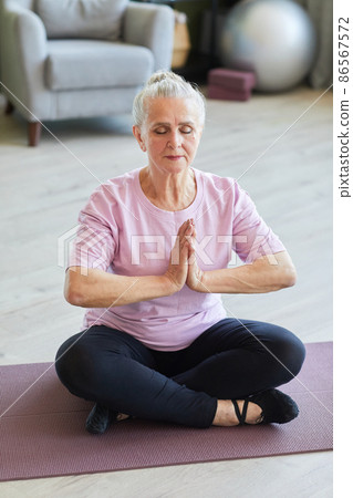 Tranquil senior sportswoman in leggins and t-shirt sitting in lotus position Tranquil senior sportswoman in leggins and t-shirt sitting in lotus position 86567572