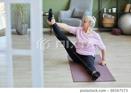 Senior active woman sitting on mat and doing stretching exercise 86567573