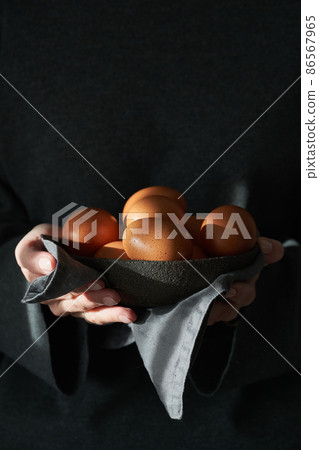 Unusual Easter on a dark background. A bowl of brown eggs with hands. Unusual Easter on a dark background. A bowl of brown eggs with hands. 86567965