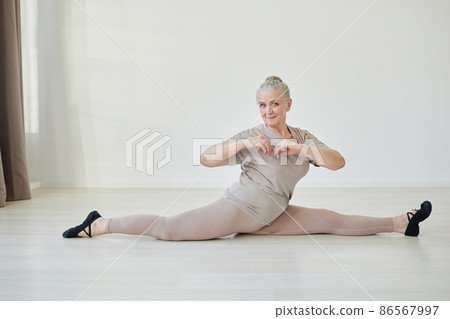 Happy mature female in light grey activewear sitting in twine Happy mature female in light grey activewear sitting in twine 86567997