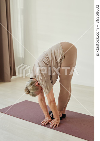 Aged retired woman in sports clothes bending forwards and turning aside Aged retired woman in sports clothes bending forwards and turning aside 86568032