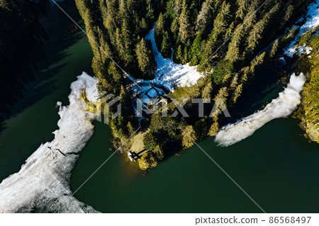 Lake Synevyr framed by a pine forest in the Carpathians, drone view, Synevyr Glade National Nature Park. Lake Synevyr framed by a pine forest in the Carpathians, drone view, Synevyr Glade National Nature Park. 86568497