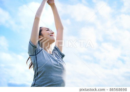 A young woman in training wear doing yoga against the blue sky 86568698
