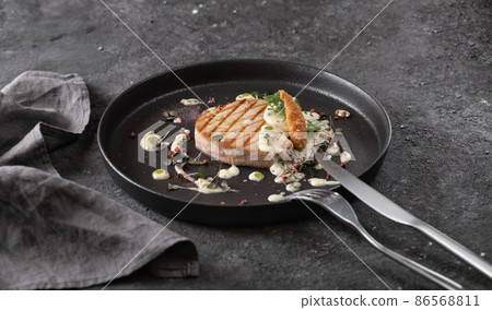 grilled tuna steak with sauce, black round plate on dark background 86568811