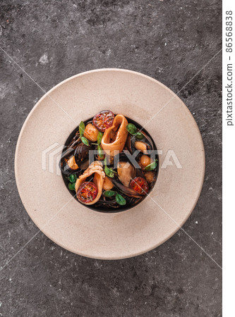 Black spaghetti pasta with black squid ink and seafood in pepper sauce and parmesan. Gray background. Black spaghetti pasta with black squid ink and seafood in pepper sauce and parmesan. Gray background. 86568838
