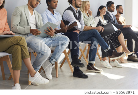 Crop image of diverse employees sit on chairs in row listen to seminar or training in office. Job candidates or applicants in line wait for interview for vacant position. Employment, hiring concept. Crop image of diverse employees sit on chairs in row listen to seminar or training in office. Job candidates or applicants in line wait for interview for vacant position. Employment, hiring concept. 86568971
