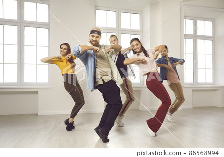Energetic diverse group of dancers in casual clothes learn moves on lesson or class in studio. Smiling young people dance prepare for concert or performance in club. Hobby and entertainment concept. 86568994
