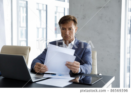Focused mature company executive reviewing sales reports 86569396