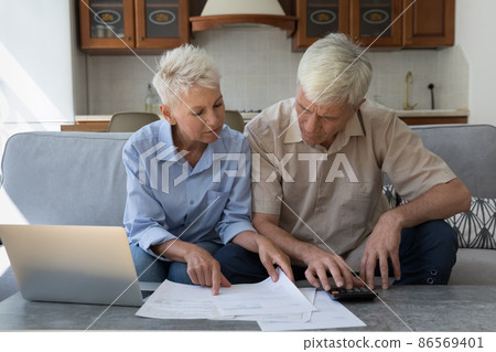 Focused older 60s husband and wife paying paper bills Focused older 60s husband and wife paying paper bills 86569401