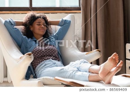 Relaxed young African American woman sleeping in cozy armchair. 86569409