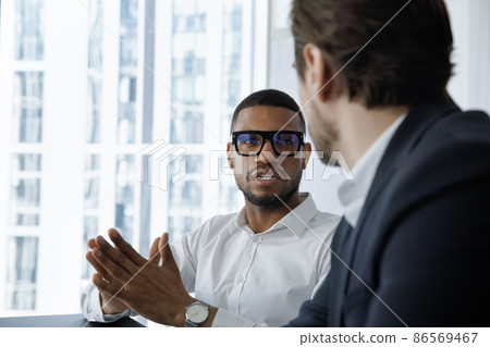 Serious engaged African employee in glasses talking to coworker 86569467
