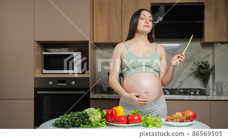 Pregnant woman peals and eats celery caressing bare belly 86569505