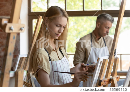 Young craft studio class student in apron drawing in paints Young craft studio class student in apron drawing in paints 86569510