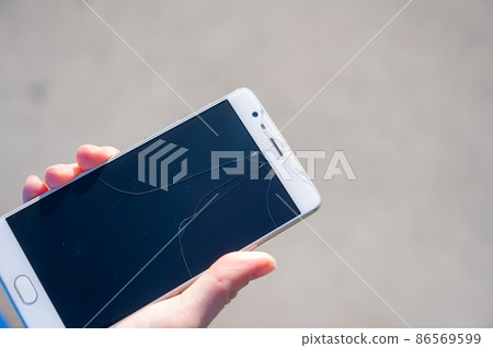 Woman holding smartphone with broken screen outdoors.  86569599