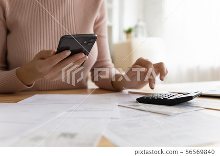 Woman makes calculations, pay bills through e-bank app on smartphone Woman makes calculations, pay bills through e-bank app on smartphone 86569840