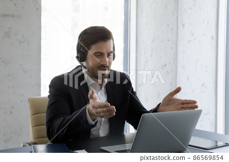 Serious business professional man in headphones with mic using laptop Serious business professional man in headphones with mic using laptop 86569854