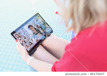 A woman by the pool holds a tablet on her lap, blurry 86570047