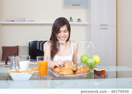 Smiling young woman eating breakfast at table in kitchen 86570048
