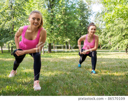 Outdoor pursuits together. Two caucasian women practise workout with dumbbells in public park in summer, selective focus Outdoor pursuits together. Two caucasian women practise workout with dumbbells in public park in summer, selective focus 86570109