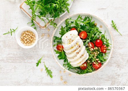Salad with arugula, mozzarella cheese and pine nuts. Breakfast. Ketogenic, keto or paleo diet. Healthy food. Top view Salad with arugula, mozzarella cheese and pine nuts. Breakfast. Ketogenic, keto or paleo diet. Healthy food. Top view 86570367