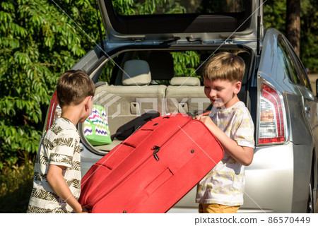 Two adorable boys holding a suitcase going on vacations with their parents. Two kids looking forward for a road trip or travel. Family travel by car 86570449